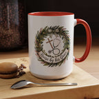 White mug with red interior and handle, featuring a design with a cross, stethoscope, and wreath, on a wooden surface with coffee beans and a macaron.